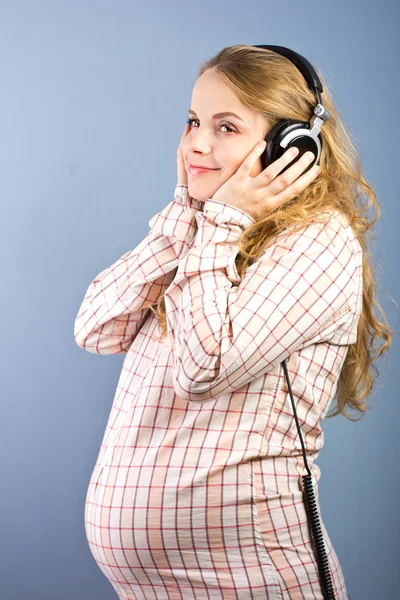 Beautiful pregnant blonde listens to classical music on headphones. Portrait of pregnant woman. The development of the child in the womb