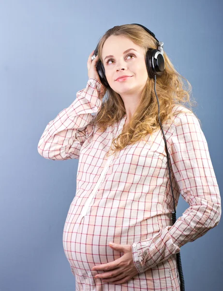 Young pregnant woman listening to music on headphones at home closed. Portrait of pregnant woman