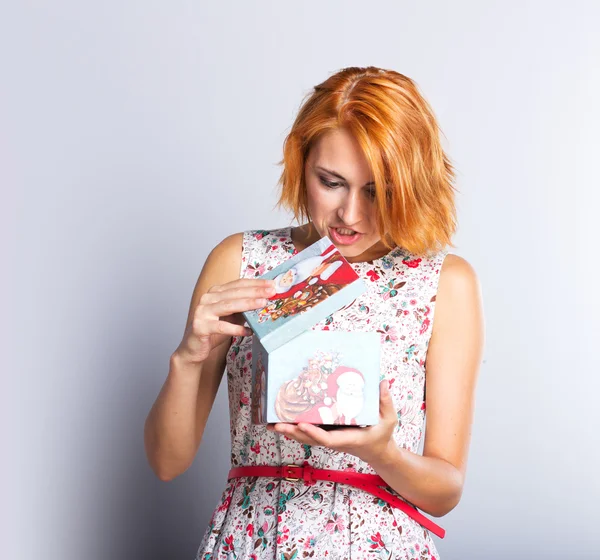 Beautiful slim girl in a short dress holding gift box. Colorful background. Portrait of red-haired girl