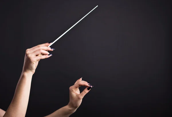 Conductor\'s baton in beautiful female hands on a black background.Conductor holds baton in the dark.