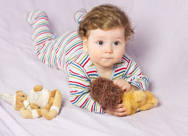 Beautiful child in crib with toys. Cute boy. Curly blonde. Portrait of a baby