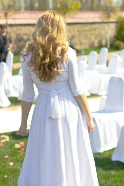 Blonde girl in a long white dress back to the the camera.