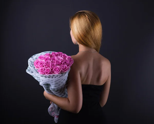 Beautiful girl with long hair with a large bouquet of roses. Long-haired girl with flowers. Gift girlfriend. Shiny hair on a black background