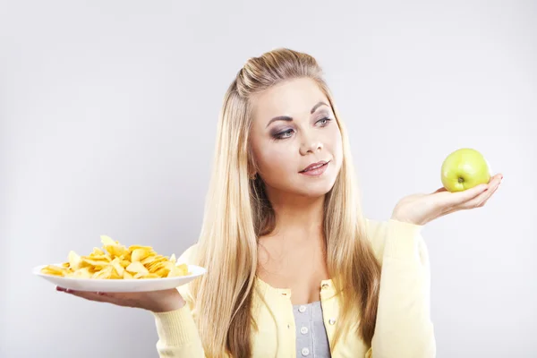 Girl chooses between an apple and potato chips. Blonde thinking what to eat.