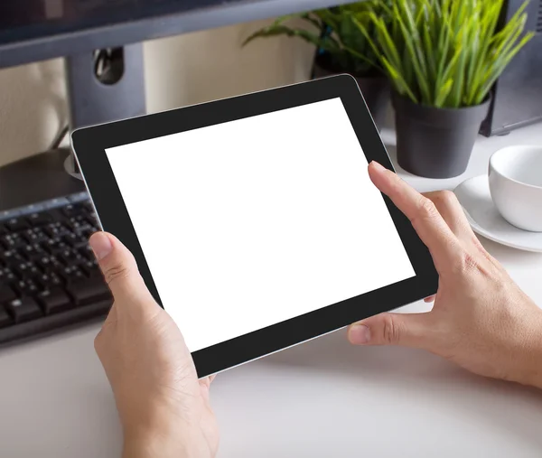 Hands of a man holding blank tablet device over a workspace tabl