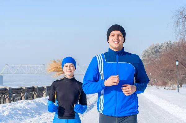 Runners. Young running couples. Sport man & woman jogging on winter embankment