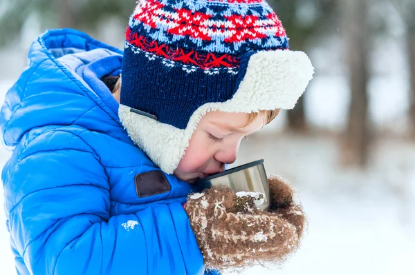 Outdoor portrait Happy child drinking hot tea from a thermos in winter park