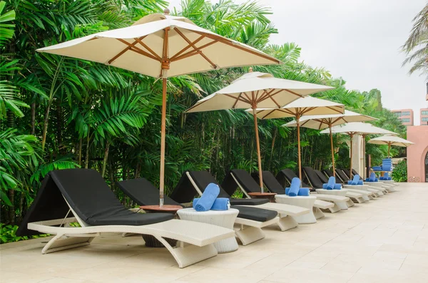 Many chairs and white umbrellas besides swimming pool