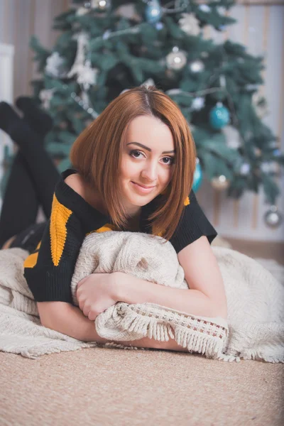 Beautiful young girl sitting on the floor on a background of green trees, she is dressed in a striped sweater, black shorts and socks. She smiles, she has red hair, big eyes, the girl on the pillow