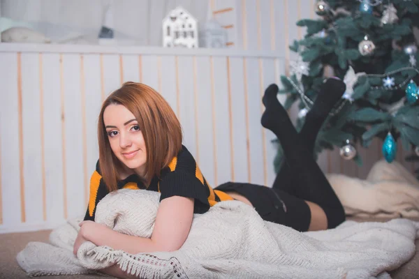 Beautiful young girl sitting on the floor on a background of green trees, she is dressed in a striped sweater, black shorts and socks. She smiles, she has red hair, big eyes, the girl on the pillow