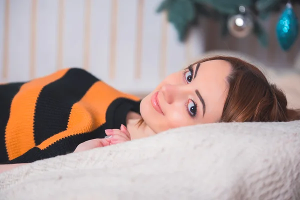 Beautiful young girl sitting on the floor on a background of green trees, she is dressed in a striped sweater, black shorts and socks. She smiles, she has red hair, big eyes, the girl on the pillow