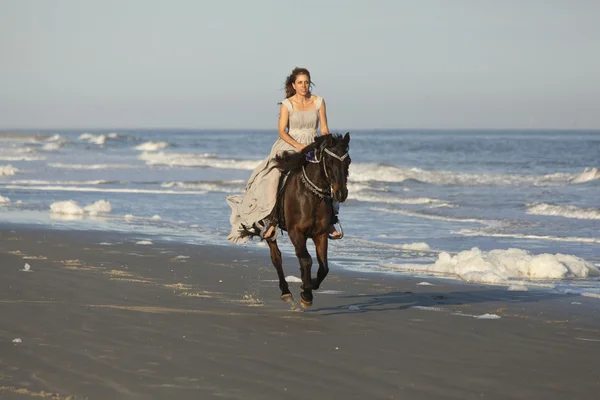 Woman in formal dress riding horse on beach