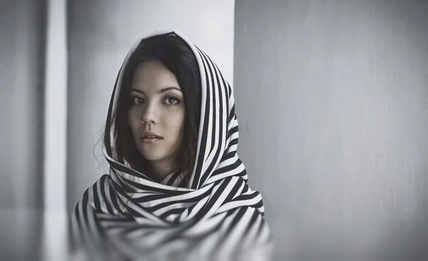 Portrait of a beautiful woman with scarf  on her head, near white wall