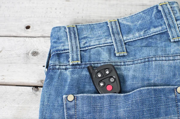 Car remote starter in blue jeans back pocket against wooden back