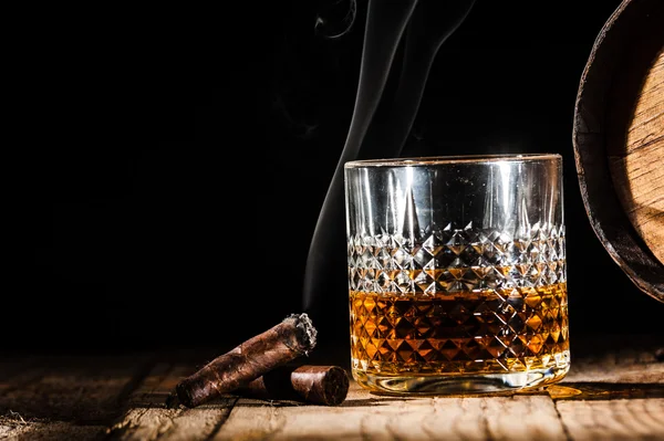 Glass of alcohol and smoking noble cigar on a black background