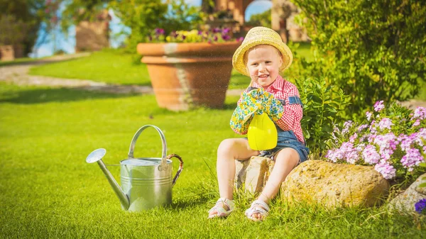 Cute little girl doing garden work between colorful flowers.