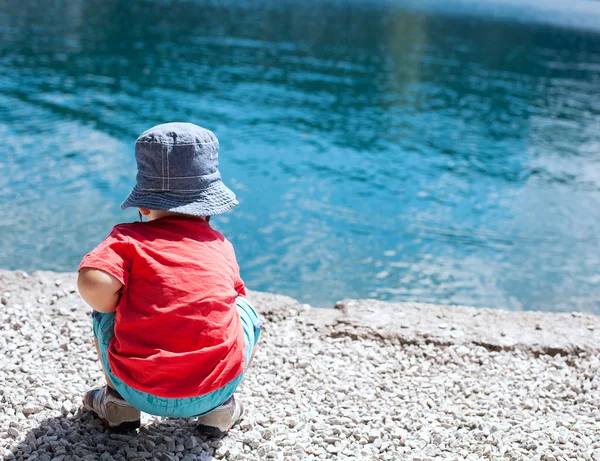 Child in summer clothes on a background of the bright blue waters of the lake. Safety near the water in the summertime.