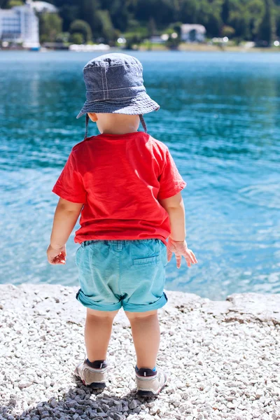 Child in summer clothes on a background of the bright blue waters of the lake. Safety near the water in the summertime.