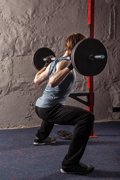 Man crouches down with barbell.