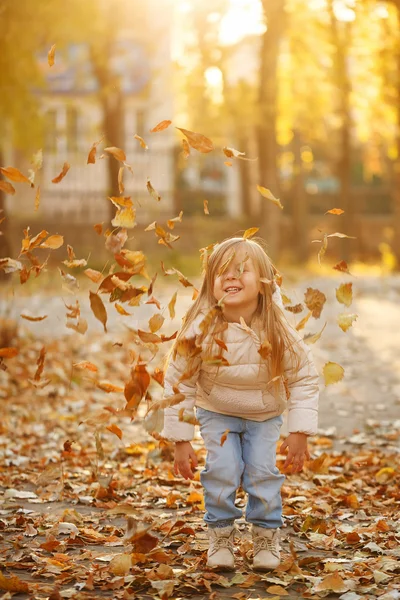 Little girl throws fallen leaves. Autumn.