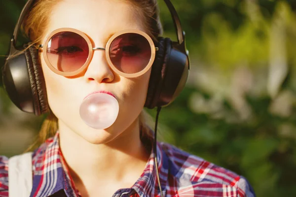 Hipster girl listening to music on headphones and chews the cud.