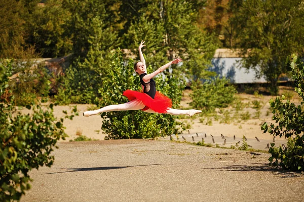 Ballerina in red tutu dancing in park. Grande pas des chat
