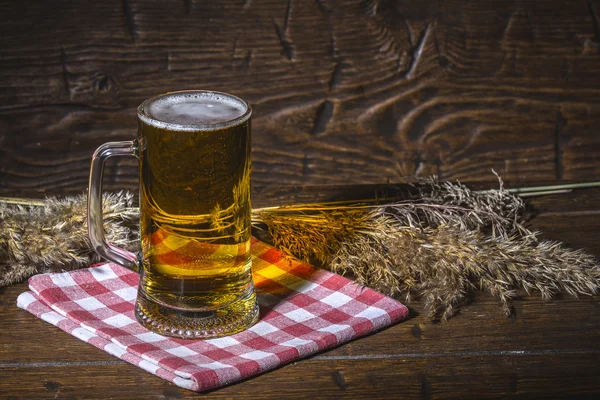 Mug of cold beer is standing on the checkered  napkin on vintage