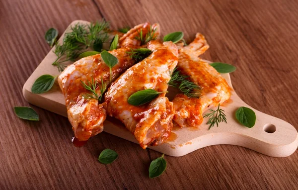 Three marinated chicken wings on wooden board