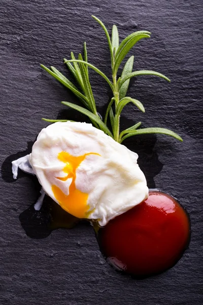 Single poached egg on black stone with herb and ketchup