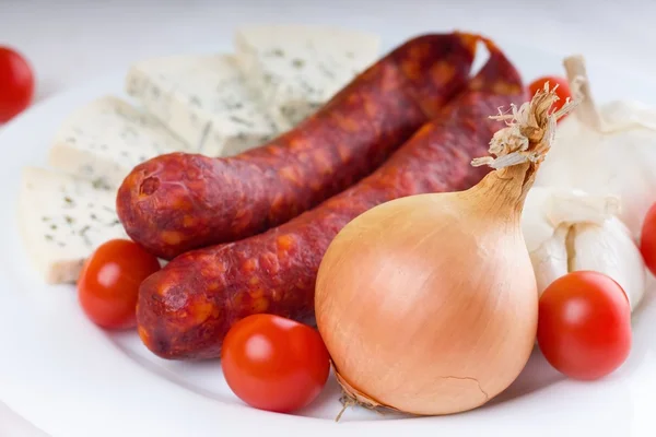 Onion and tomatoes with sausages on white plate