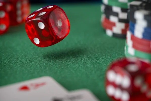 Red dice rotates in the air, casino chips, cards on green felt