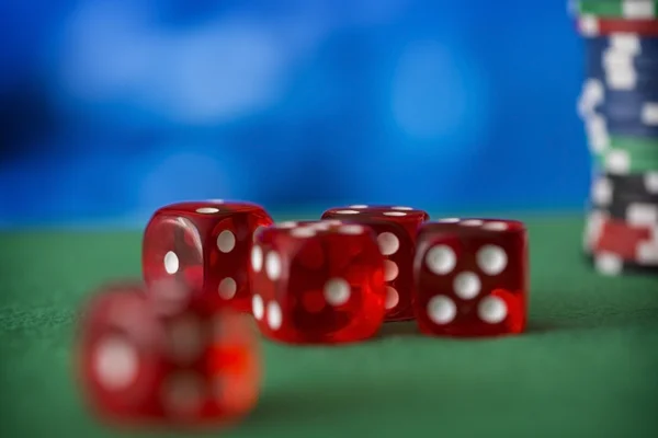 Red dice rotates on green felt, casino chips and cards