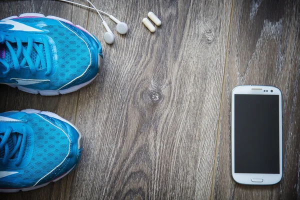 Sport shoes, phone and smart watch with set for sports activities on floor.