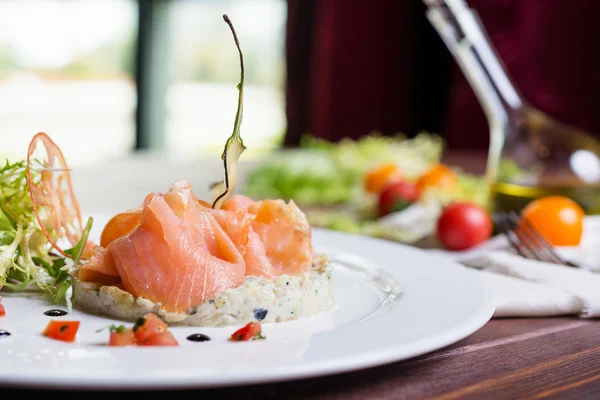 Creative composition delicious fresh smoked sliced salmon with tartar sauce on a white plate on a wooden table in a restaurant with decor