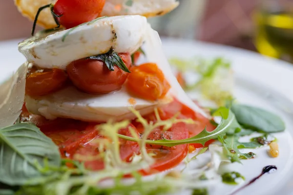 Plate of healthy classic caprese salad with mozzarella cheese, tomatoes and basil on a wooden table in a restaurant