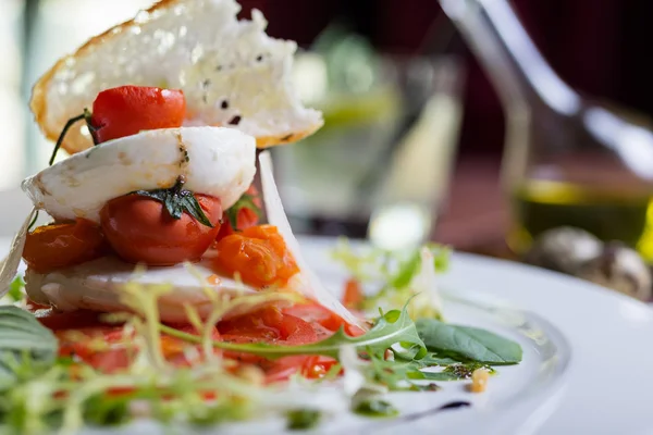Plate of healthy classic caprese salad with mozzarella cheese, tomatoes and basil on a wooden table in a restaurant