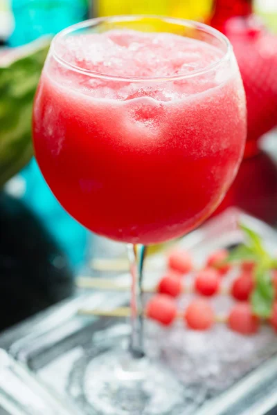 Refreshing glass of bright juicy watermelon smoothie or lemonade with ice on a table at a restaurant with the decor of the bright dishes and pieces of watermelon