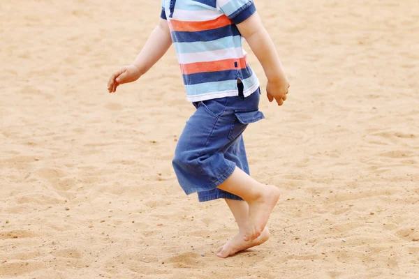 Legs od barefoot of little boy in shorts running on sand at summ