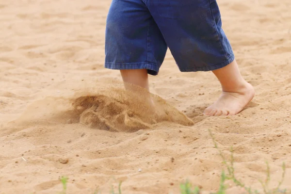 Legs of barefoot of little boy in shorts running on sand, close