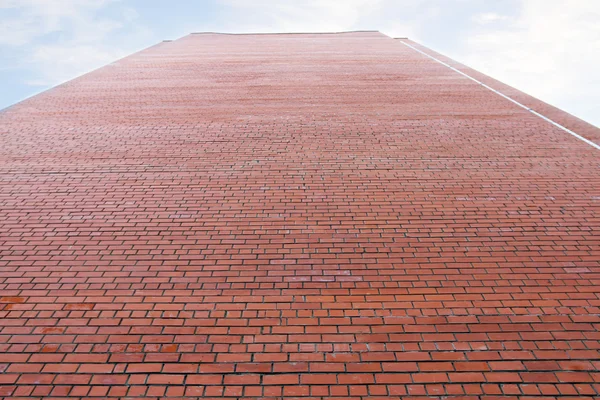 Very high wall of red brick building and cloudy sky high above