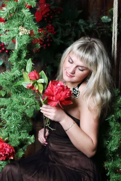 Beautiful young woman sits on swing and holds flower in room wit