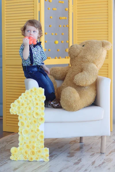 Little handsome happy boy stands on soft armchair with big bear