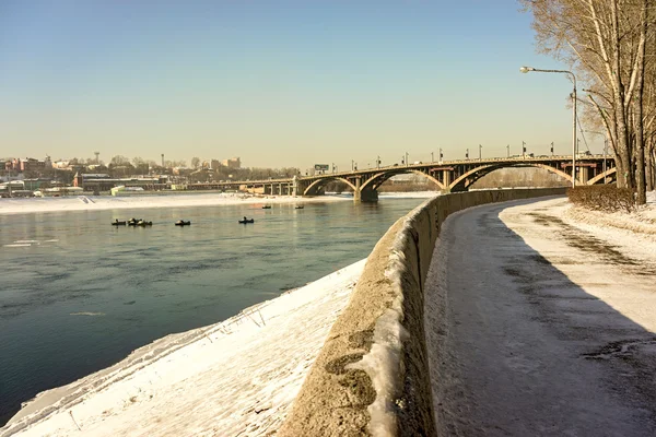 Eastern Siberia, Irkutsk. Angara pure water in winter day. Old bridge over the river, which is constructed in 1936. Group of boats with fishermen.