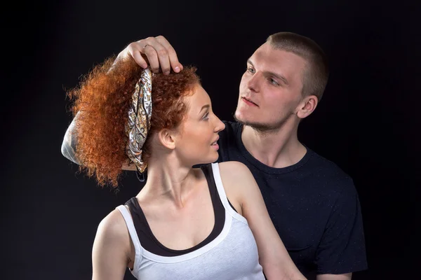 Fashionable couple posing at studio. Man corrects a handkerchief on woman\'s head.