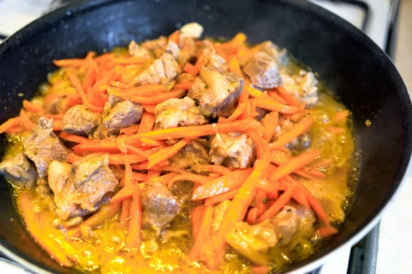 Cooking meat with carrot in frying pan