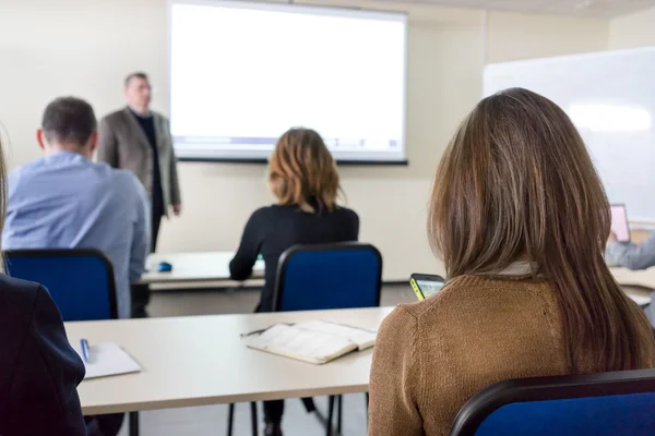 People sitting rear at the desks in the education class and the lecturer near the white desk