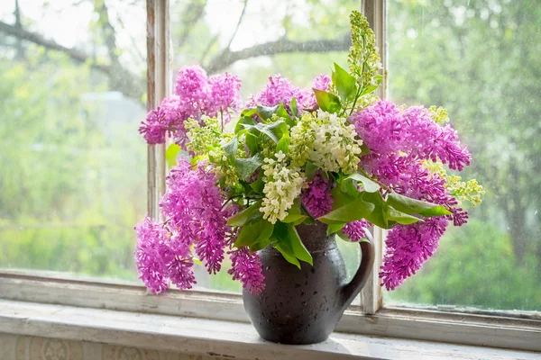 Bouquet of lilac in a brown clay vase on a window sill