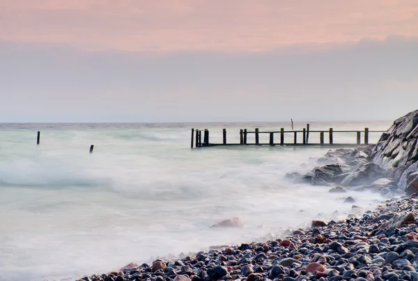 Abandoned wooden wharf in sea within sunrise.Gentle blue pink color of sky, blur waves