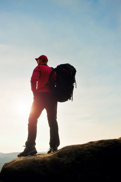 Tall tourist red black sportswear. Sunny evening in rocky mountains. Hiker with big backpack stand on rocky view point