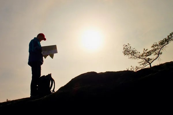 Silhouette of young man looking at a map in nature while hiking